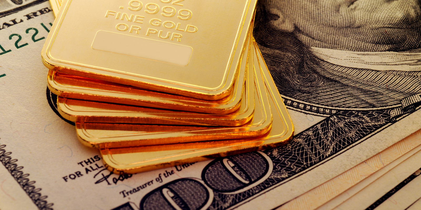 gold ingots displayed on top of 100 dollar bills